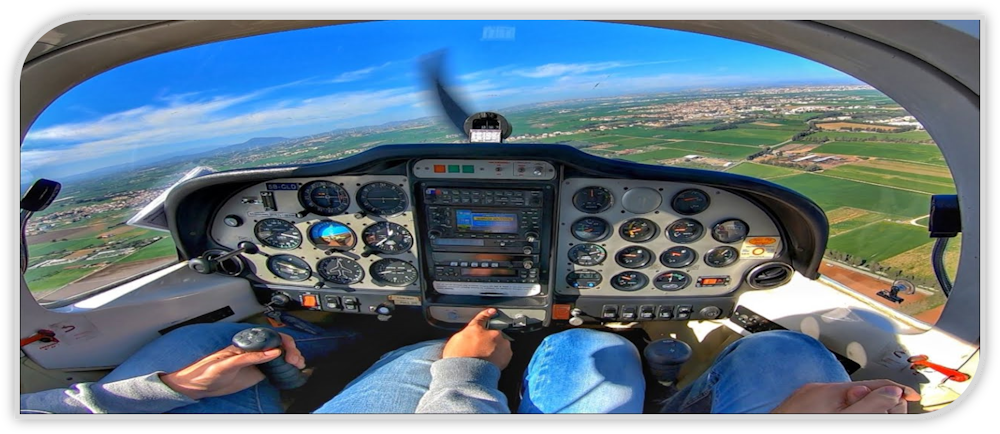 A point-of-view perspective of sitting in the cockpit of a small plane, flying over green meadows on a clear and sunny day